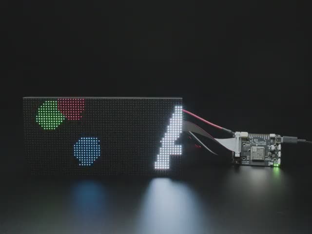 Video of Adafruit Matrix Portal S3 linked up to a matrix displaying the "Adafruit Matrix Portal" in white letters and red, green and blue circles jumping around. 