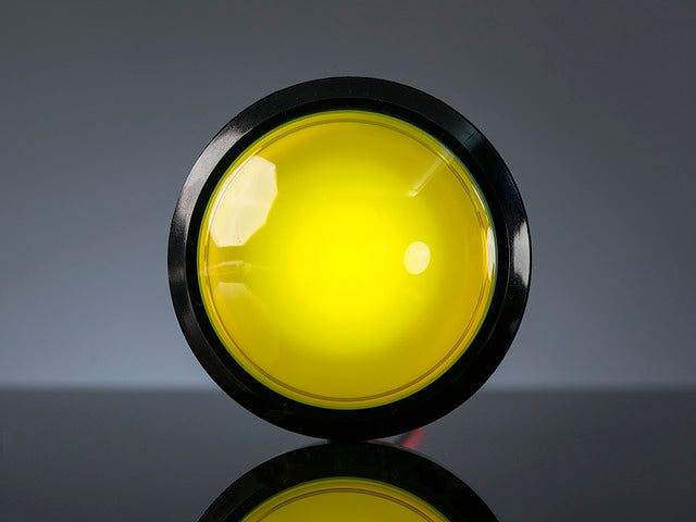 Head-on shot of illuminated massive yellow 100mm arcade button.