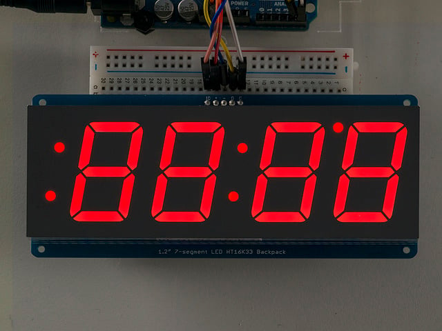 Huge red 7-segment clock display soldered to backpack with all segments lit