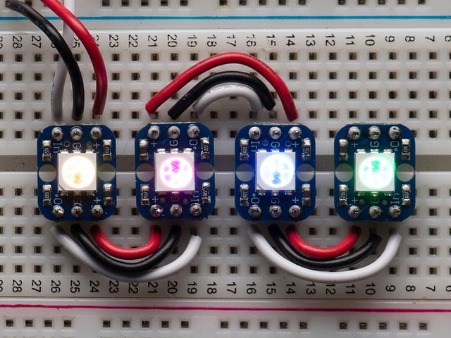 Four glowing Breadboard-friendly RGB Smart NeoPixels wired up on a breadboard