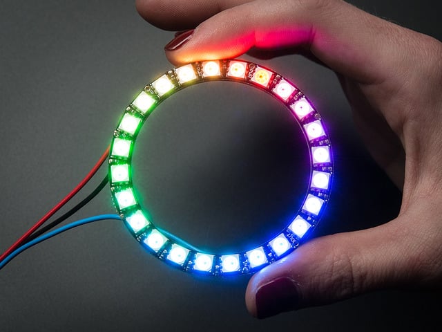 Hand holding NeoPixel Ring with 24 x 5050 RGB LED, lit up rainbow