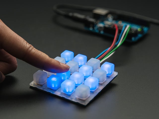 Finger pressing a button on lit up elastomer button pad