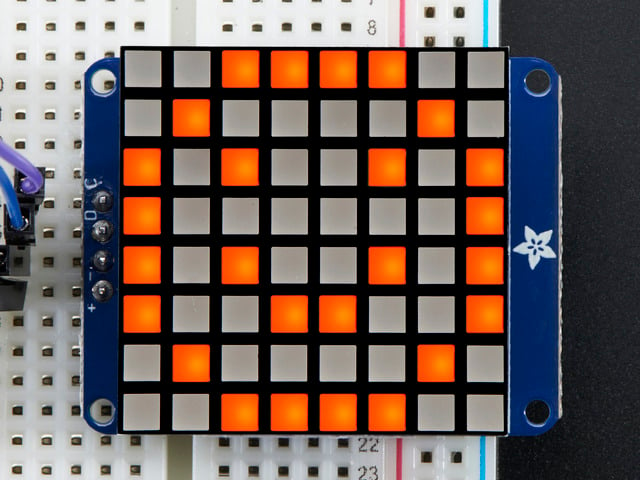 Close-up of Soldered and assembled Small 1.2" 8x8 Ultra Bright Square Amber LED Matrix + Backpack on a breadboard powered by an Arduino Uno. The LED Matrix displays an orange smiley.