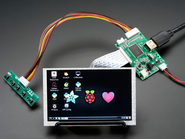 Angled shot of an assembled HDMI 4 Pi: 5" Display (no Touch) w/Mini Driver. The HDMI screen displays a desktop image including the Adafruit logo, the Raspberry Pi logo, and a pink heart.