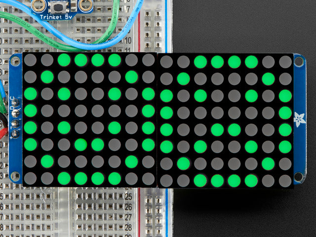 Close-up of Soldered and assembled 16x8 1.2" LED Matrix + Backpack - Ultra Bright Round Green LEDs on a breadboard. The LED Matrices display a smiling emoji and a frowning emoji.