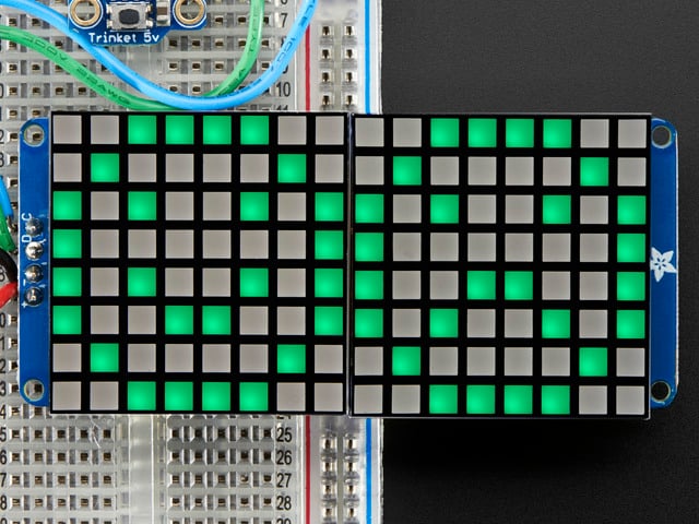 Close-up of Soldered and assembled 16x8 1.2" LED Matrix + Backpack - Ultra Bright Square Green LEDs on a breadboard. The LED Matrices display a smiling emoji and a frowning emoji.