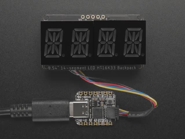 Overhead shot of an assembled 14-segment LED backpack, emitting the follow text in yellow LEDS: "AdaFruit 14-Segment Backpack"