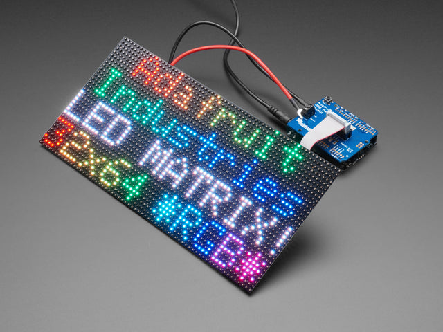 Adafruit RGB Matrix Shield for Arduino connected to a LED Matrix that reads "Adafruit Industries LED MATIX! 32x64 *RGB*"