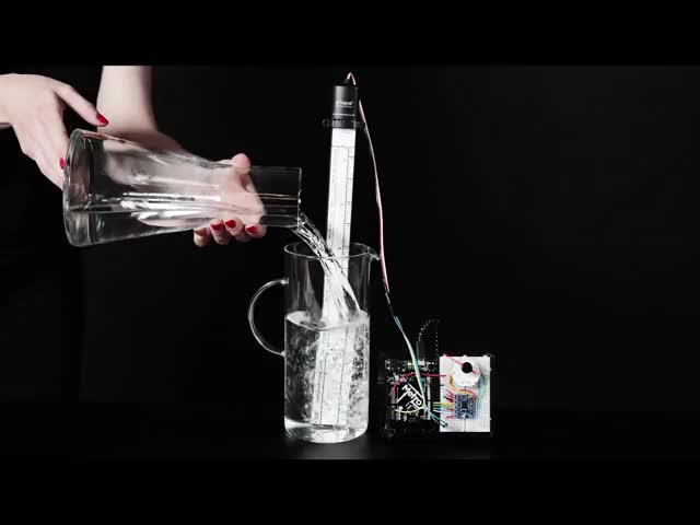 Hand pouring water into tall carafe with water sensor inside it, a gauge increases as more water is poured