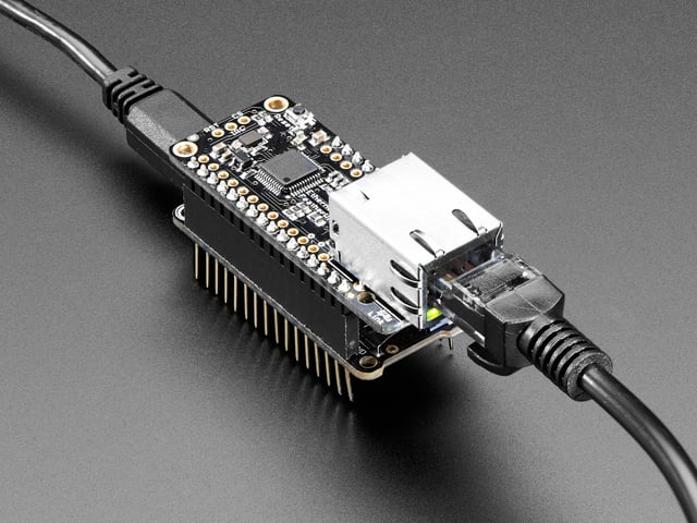 Angled shot of a Adafruit Ethernet FeatherWing with an Ethernet cable connected to it. 