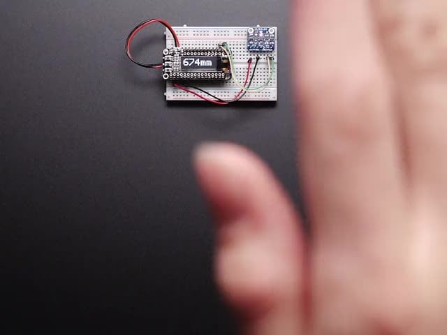 Video of a white hand hovering over a Adafruit VL53L0X Time of Flight Distance Sensor that's connected to a white breadboard reading the range of motion of the white hand. 