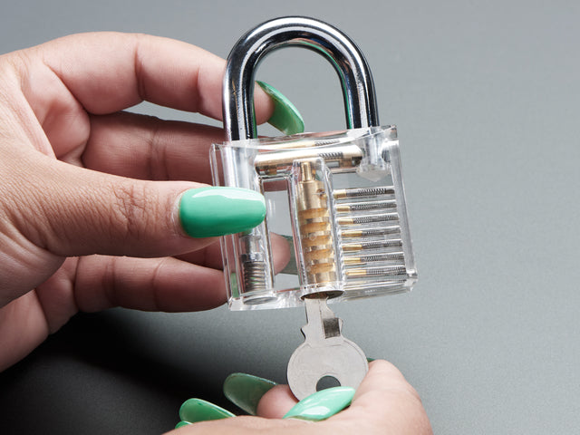 Hands holding clear padlock and opening with a small key.