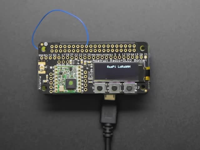 A rectangular microcontroller with OLED screen. A blue-manicured index finger presses buttons below the OLED screen, triggering different texts.