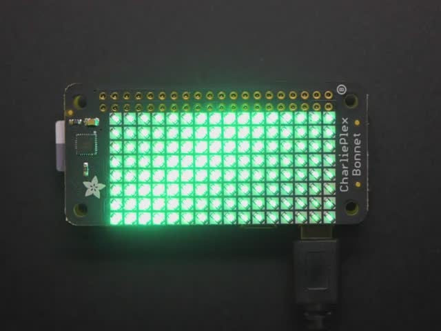 Top down view of a Adafruit CharliePlex LED Matrix Bonnet illuminating green. 