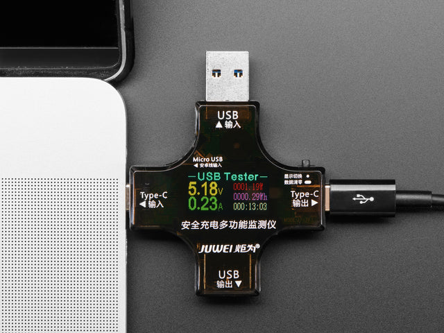 Top view of multifunctional USB tester connected to a laptop. The display reads voltage and current information.