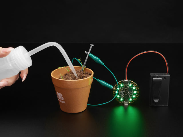 Person watering sprouts with a Circuitry water sensor attached