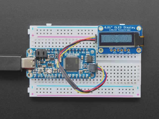 Monochrome OLED module wired to Feather showing text and circles