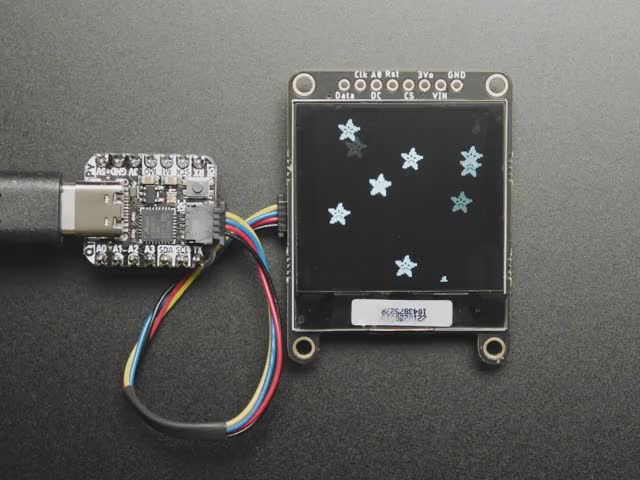 Monochrome OLED module wired to QT Py showing falling Adafruit logos