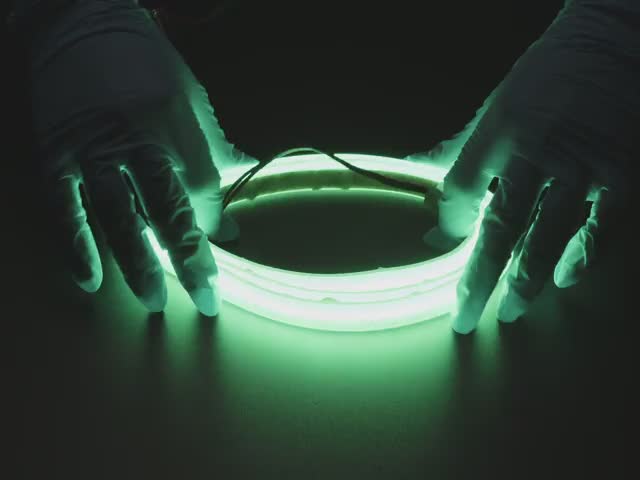 Two hands repeatedly bending and manipulating lit-up flexible green LED strip