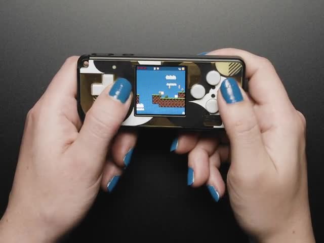 Video of a white person with blue painted nails playing a handheld gaming console.