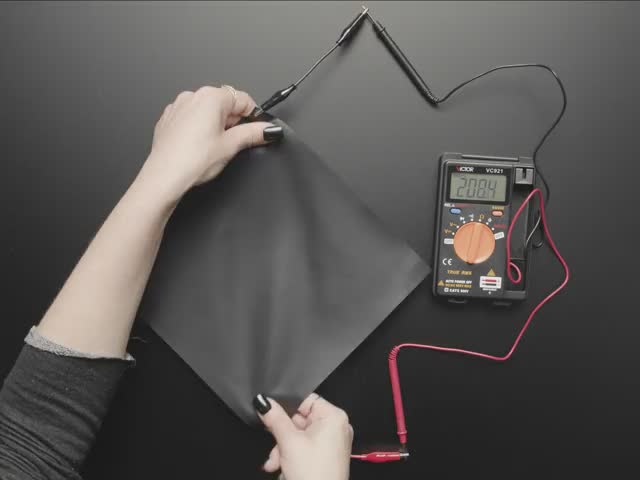 Video of a pressure-sensitive conductive sheet pulled by the corners, which are clipped to alligator test leads and a multimeter. The multimeter displays the fluctuations in resistance.