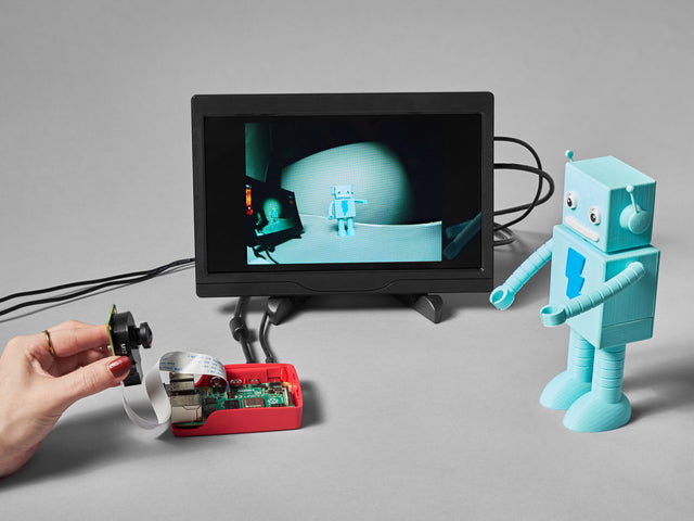 Lifestyle image of a friendly robot figurine used as a Raspberry Pi camera module subject. The lens on the camera is wide angle.