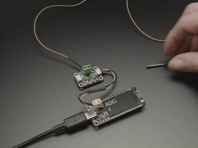 Video of a white hand squeezing a thermocouple. The digital readout is on a TFT display on a long, rectangular microcontroller.