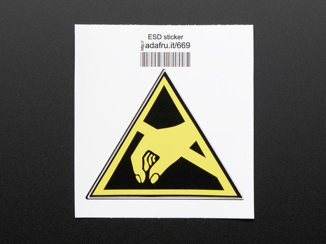 Triangle shaped sticker with yellow hand reaching to pick something up, over a black background, with yellow trim. Mounted on white paper with barcode