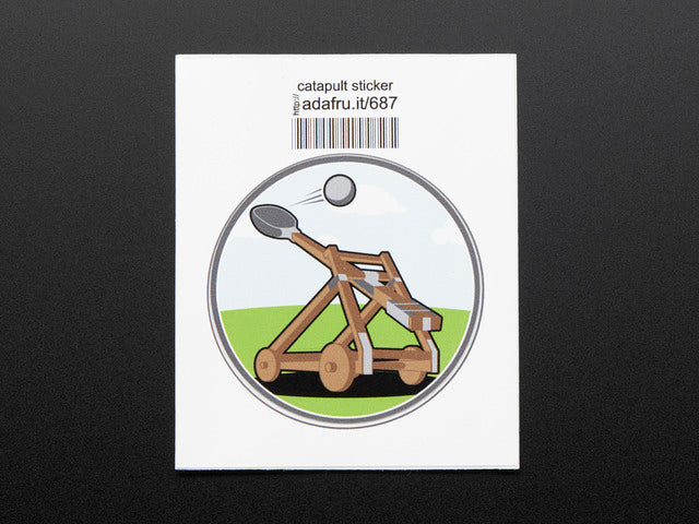 Circular sticker with brown catapult mid-fling, over an abstracted blue sky and green grass background. Sticker is trimmed in grey and mounted on white paper with barcode.  