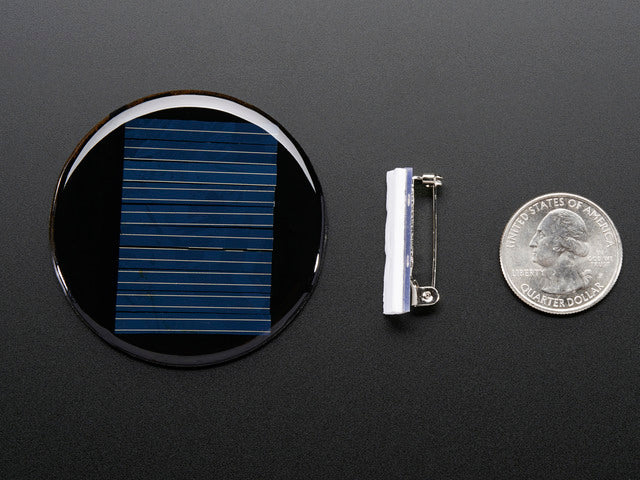 Round solar panel next to lapel pin and quarter