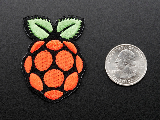 Embroidered patch in the shape of the raspberry pi logo, in red with green leaves on top, outlined in black. Shown next to quarter for scale. 